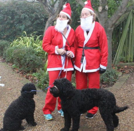 two women in Santa costumes with two black dogs 