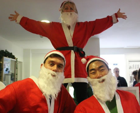 man standing behind two others, all dressed as Santa 
